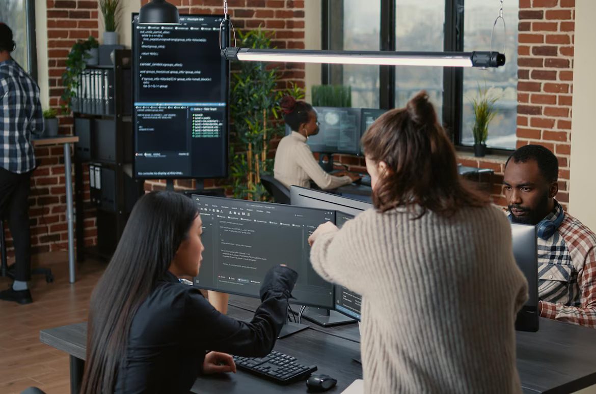 software-programer-pointing-pencil-source-code-computer-screen-explaining-algorithm-coworker-standing-desk-programmers-discussing-online-cloud-computing-with-team (1)