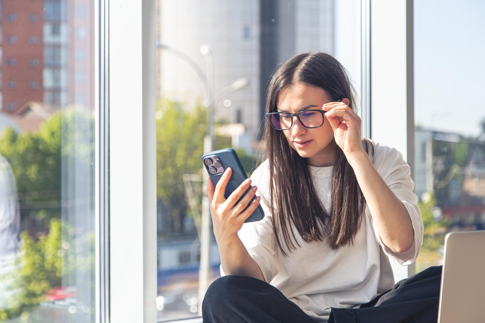 young-woman-with-smartphone-front-laptop-screen-office young-woman-with-smartphone-front-laptop-screen-office